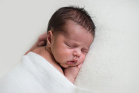 Newborn baby sleeping on a white blanket resting his head on his hand
