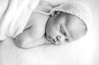Newborn baby sleeping on a white blanket with a knitted bonnet