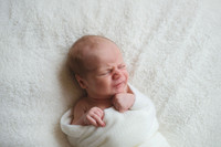 Newborn baby wrapped on a white blanket pulling a face
