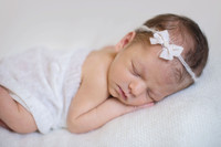 newborn baby sleeping on a white blanket with a white bow headband