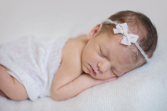newborn baby sleeping on a white blanket with a white bow headband