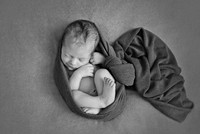 Black and white photo of a newborn baby wrapped up in a soft flowing swaddle