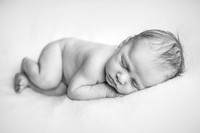 Black and white photo of a newborn baby sleeping on a white blanket