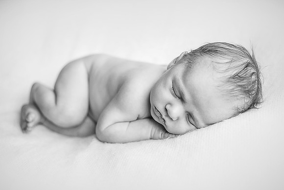 Black and white photo of a newborn baby sleeping on a white blanket