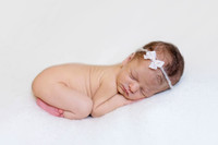 Newborn baby sleeping on a white blanket with a white bow headband