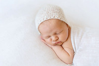 Newborn baby sleeping on a white blanket wearing a white knitted bonnet