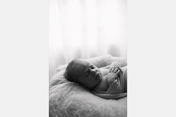Black and white photo of a newborn baby sleeping by a light filled window