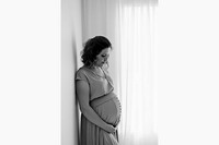 black and white photo of a pregnant woman cradling her bump backlit by a window