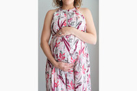 A pregnant woman with her hands around her belly wearing a floral dress
