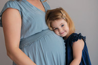 A little girl resting her head on her mums pregnant belly smiling